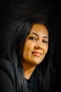 A portrait of a confident woman with a slight smile and long black hair, wearing a black blazer.